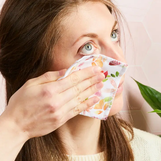 Cotton make up squares shown being wiped on a face, in watercolour design (white background with colourful flowers)