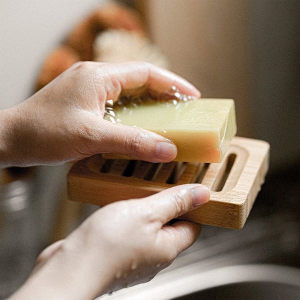 Bamboo soapdish shown held in a hand with a bar of soapy soap