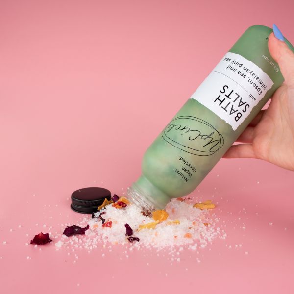 UpCircle bath salts in green glass bottle with contents being poured out showing salts and rose petals