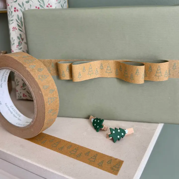 Christmas paper tape brown with green Christmas trees shown on roll next to a parcel wrapped in green paper with the tape making a decorative shape