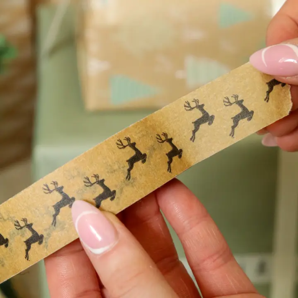 Christmas paper tape brown with black reindeers shown on roll with someone pulling the tape off the roll