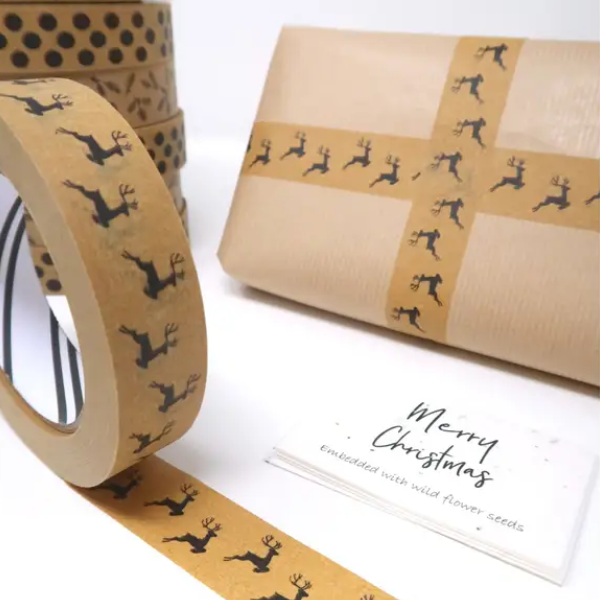 Christmas paper tape brown with black reindeers shown on roll next to a parcel wrapped in brown paper with the tape making a decorative cross