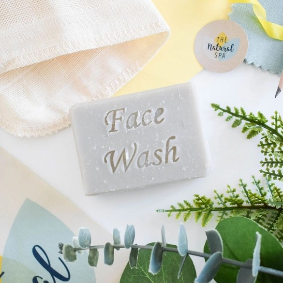 Travel facial soap bar (exfoliating) shown with greenery and a facecloth, the words 'Facial wash' stamped on the bar