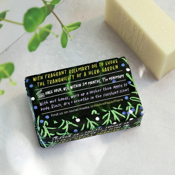 Herb garden rosemary soap bar shown wrapped (back view with text reading "with fragrant rosemary oil to evoke the tranquillity of a herb garden") alongside an unwrapped bar
