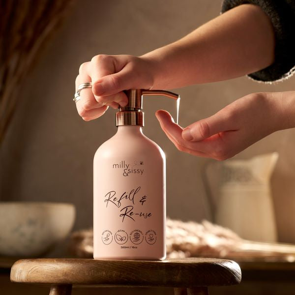 Refillable aluminium bottle in blush pink with a hand pressing the pump with product coming out