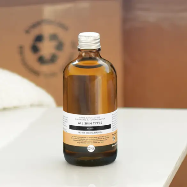 Men's micellar water and toner in dark brown glass bottle with aluminium lid on a white surface with cardboard in background