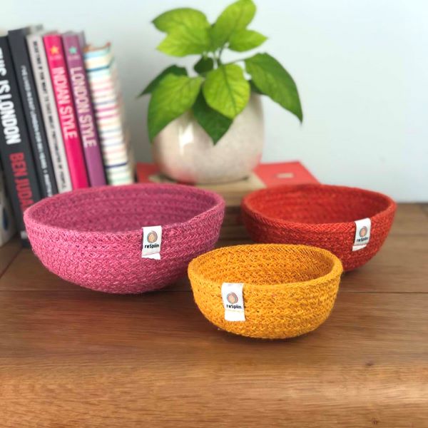 Set of three mini jute bowls in Fire colour (bright pink, orange and yellow) sitting on a wooden tabletop