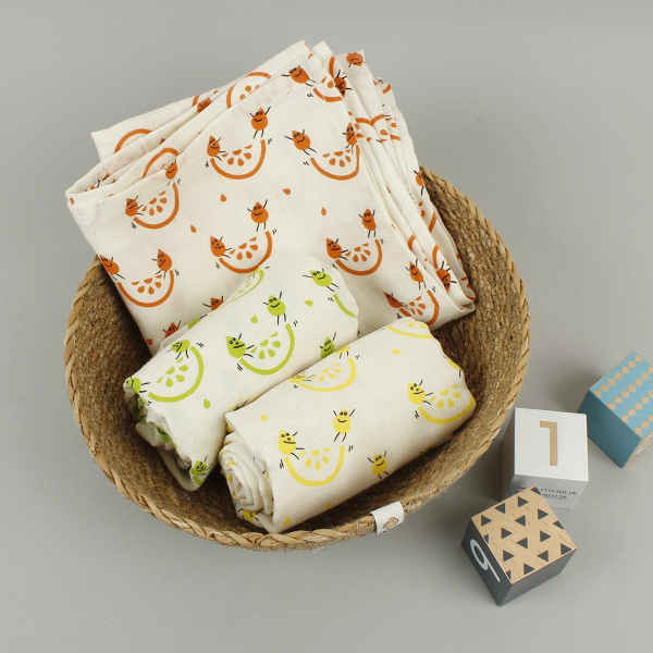 Organic cotton set of three muslin cloths, shown inside a basket with wooden child's blocks alongside. All with cream background with colourful fruity images.