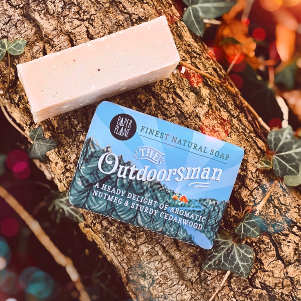 The Outdoorsman soap bar sitting on a log showing soap bar alongside a wrapped soap bar