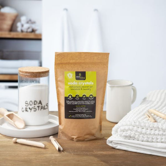 Soda crystals in paper kraft bag shown next to a glass jar containing powder with words 'soda crystals' written in pen next to some laundry