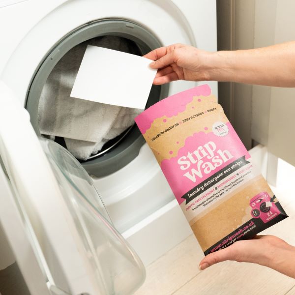 Laundry detergent strip being popped in washing machine for machine washing