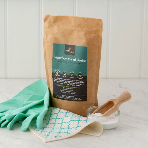 Bicarbonate of soda in kraft packaging with label reading 'all-purpose cleaner', next to gloths, natural rubber gloves and a wooden scoop