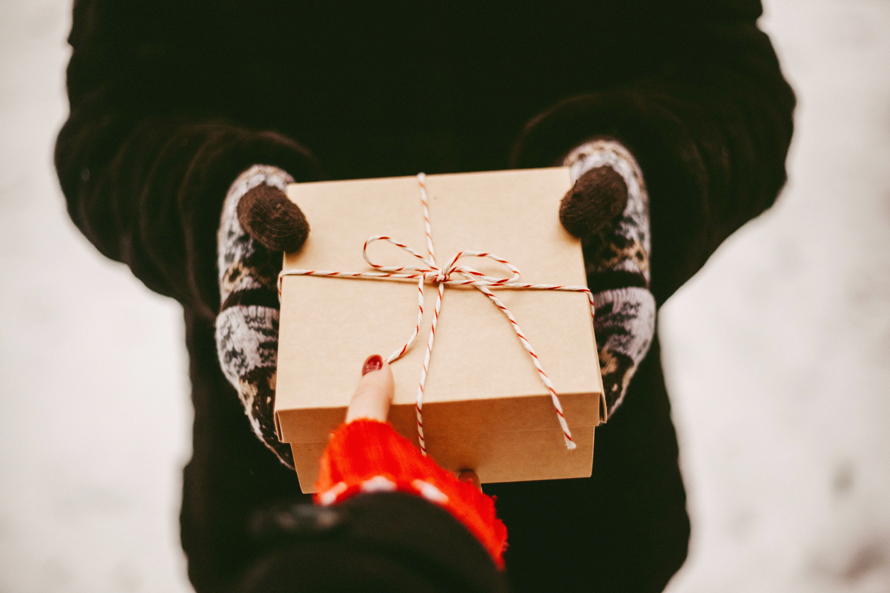 A gift in a cardboard box with a twine ribbon being passed from one person to another