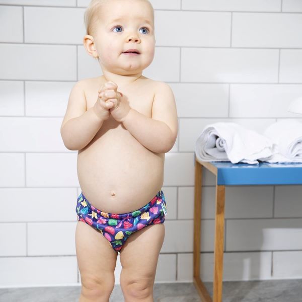 Baby wearing reusable swim pants front view in Mussel Seashell design (navy blue background with colourful starfish, mussels and shells)