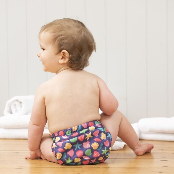 Baby wearing reusable swim nappy , in Mussel Seashells design (dark blue background with colourful star fish, mussels and shells)