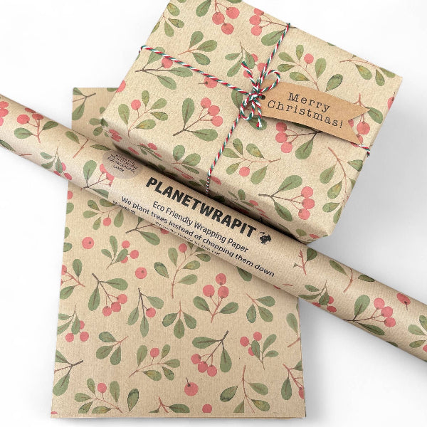 PlanetWrapIt recycled kraft wrapping paper in Christmas mistletoe (brown paper with printed red berries and green leaves) with PlanetWrapIt paper label alongside a wrapped parcel