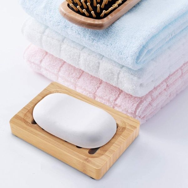 Bamboo soapdish shown holding a white bar of soap next to some towels and a hairbrush