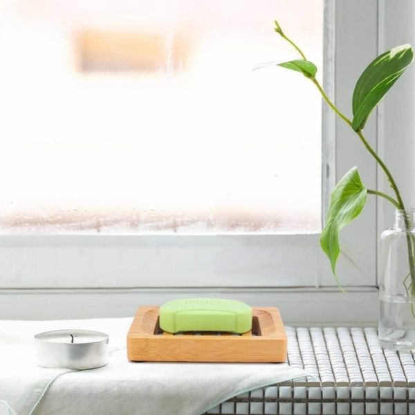 Bamboo soapdish shown holding a green bar of soap on a bathroom windowsill