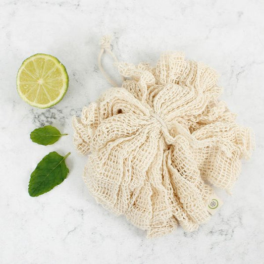 Organic cotton bath puff shown on marble work surface next to some lime and leaves