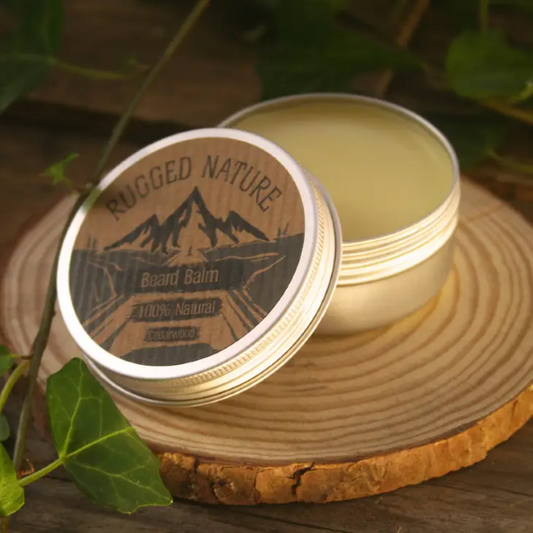 Rugged Nature beard balm in cedarwood on a piece of wood with come greenery. Aluminium lid is open showing balm inside. 