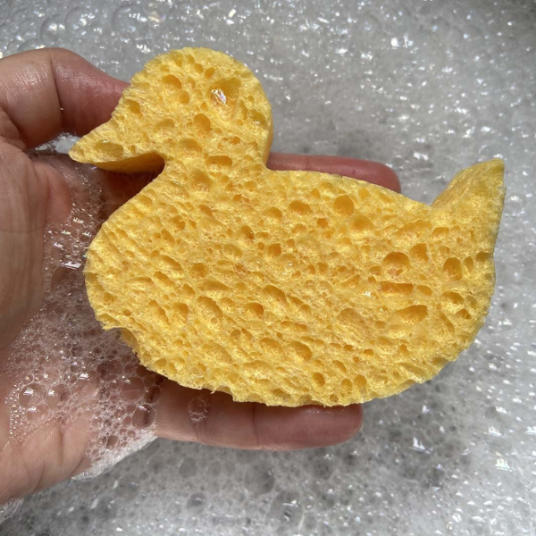Cellulose sponge in shape of a duck shown in the palm of a hand in soapy water