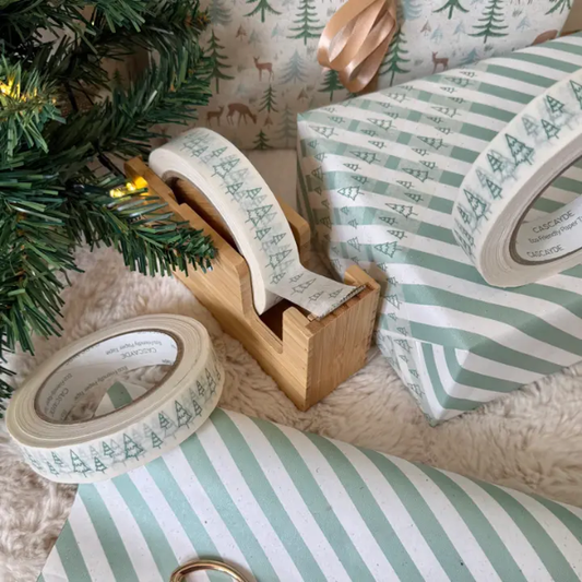 Christmas paper tape white with green Christmas trees shown on roll in bamboo dispenser next to a parcel wrapped in green striped paper with the tape attached
