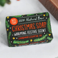 Christmas soap bars shown wrapped in paper with festive decoration reading "100% natural bar, Christmas soap, warming festive scent, cinnamon essential oil"
