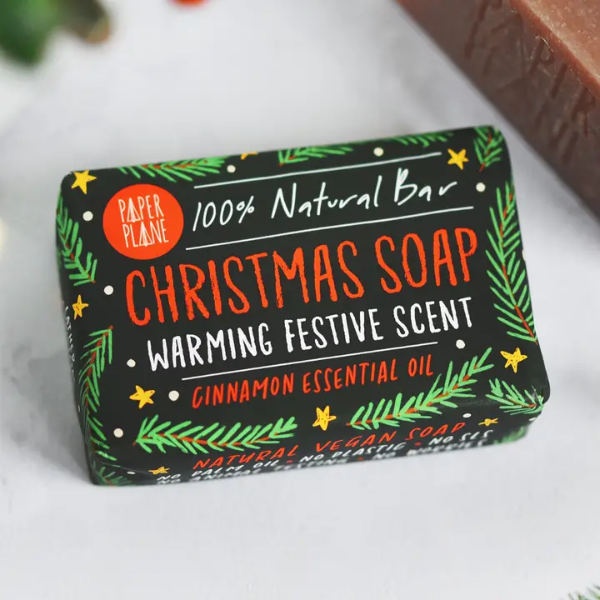 Christmas soap bars shown wrapped in paper with festive decoration reading "100% natural bar, Christmas soap, warming festive scent, cinnamon essential oil"