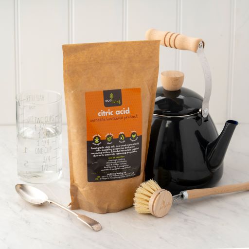 Natural citric acid in kraft paper poch shown next to a wooden dish brush, black kettle, measuring  and spoon