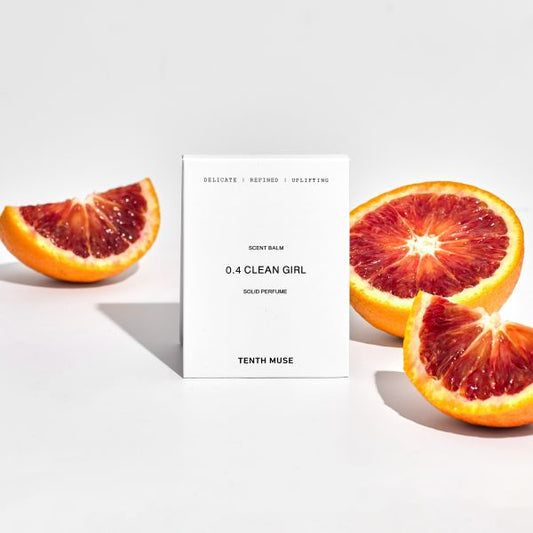 Perfume balm in white cardboard packaging with packaging reading "Delicate/Refined/Uplifting Clean Girl solid perfume" shown alongside blood oranges cut in half