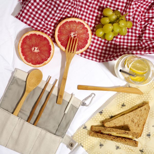 Bamboo cutlery set with chopsticks, straw and straw cleaning brush shown alongside picnic sandiwchers and fruit