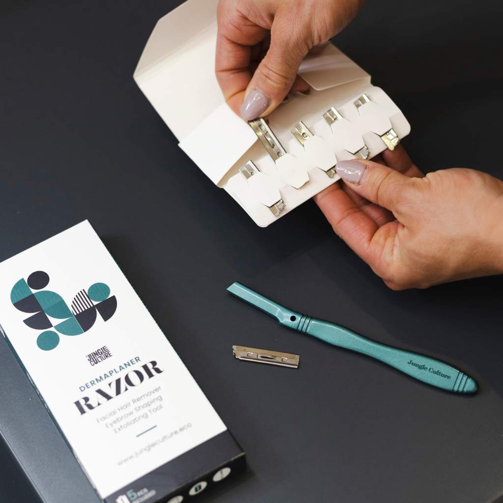 Jungle Culture's dermaplaner replacement razor blades in cardboard packaging next to a dermaplaner