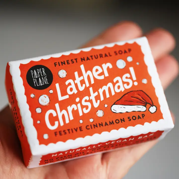 Lather Christmas soap bar shown wrapped in paper with festive decoration held in hand