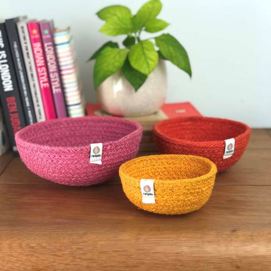 Set of three mini jute bowls in Fire colour (bright pink, orange and yellow)  sitting on a wooden tabletop