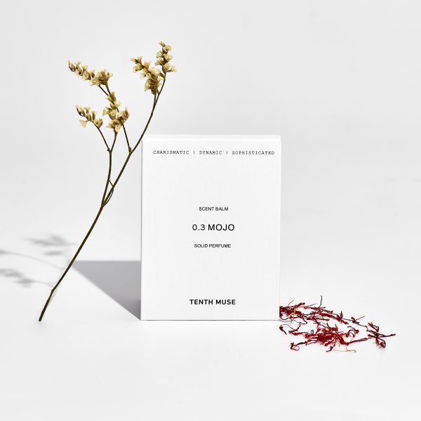 Perfume balm in white cardboard packaging with packaging reading "Charismatic/Dynamic/Sophisticated Mojo solid perfume" shown alongside dried flowers