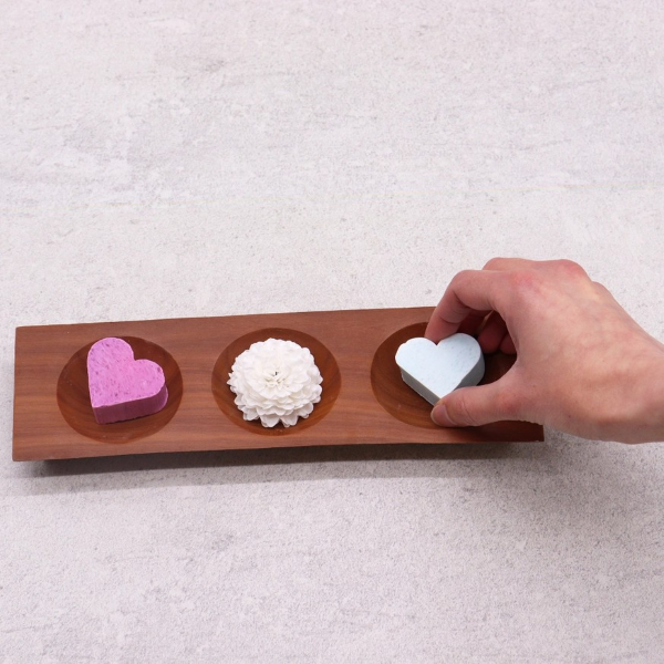 Naseberry wood three bay soapdish with three small, colourful soaps, a hand placing the third on the soapdish