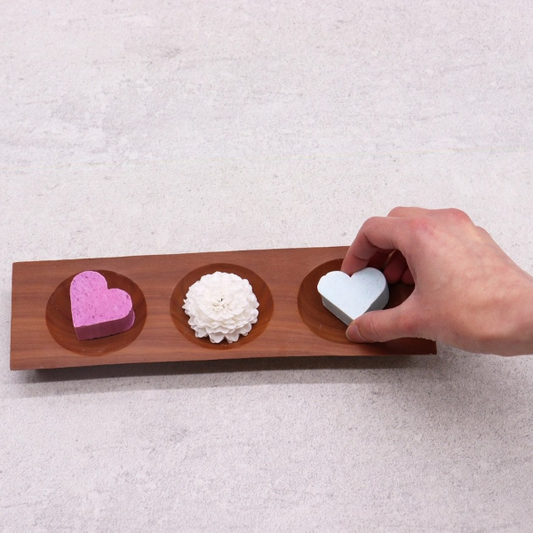 Naseberry wood three bay soapdish with three small, colourful soaps, a hand placing the third on the soapdish