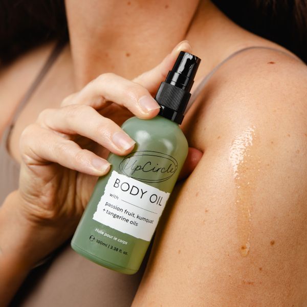 Person applying a bottle of UpCircle Body Oil to their shoulder