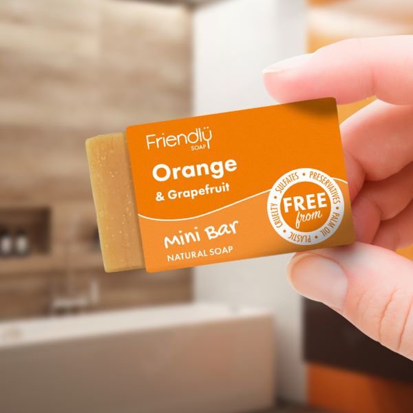 A mini vegan soap bar by Friendly Soap, orange and grapefruit scent, shown in a hand holding its orange box, the soap peeking out.