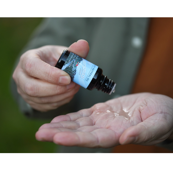 The Outdoorsman bear oil in glass bottle in a person's hand with product splashing on hand