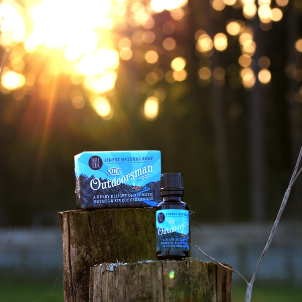 The Outdoorsman bear oil in glass bottle sitting atop a wooden post alongside The Outdoorsman soap bar