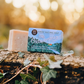 The Outdoorsman soap bar sitting on a log and some foliage
