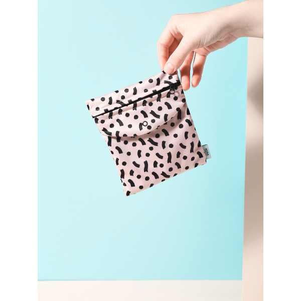 Period pad bag for out and about in Latte Wiggle design (beige background with black splashes), held in a hand
