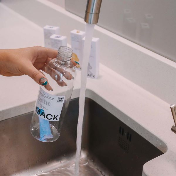 Mack cleaning pod in bottle being filled up with water at a sink