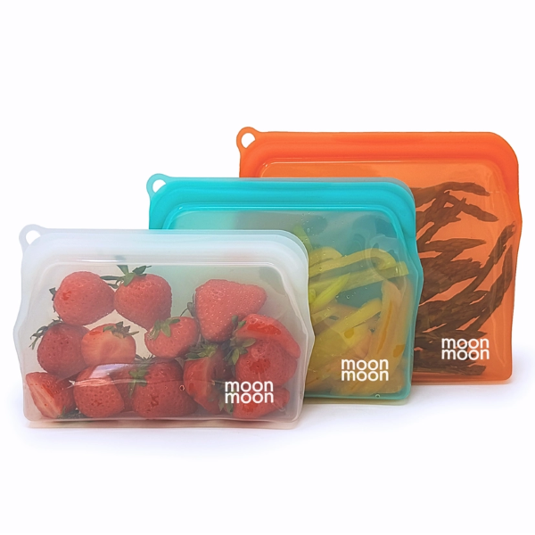 Moonmoon reusable silicone food bags, showing three sizes of bags side by side (small, white with strawberries inside, medium aqua with sliced yellow peppers and orange large with asparagus)