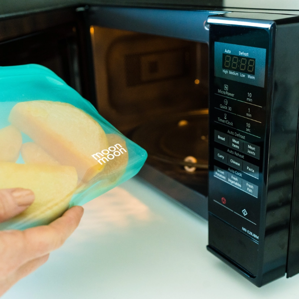 Moonmoon reusable silicone food bag in aqua being put inside a microwave