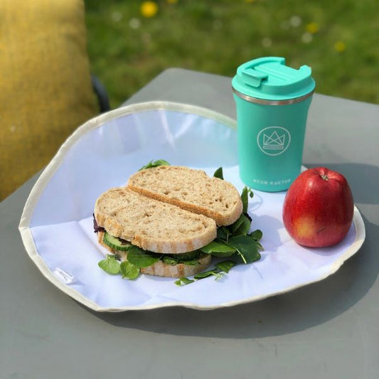 Organic cotton sandwich wrapper shown open with a sandwich, alongside Neon kactus insulated cup and an apple