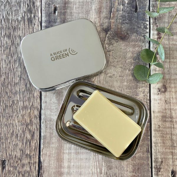 Travel soap or snack tin with lid shown off to see ridged base inside with a bar of soap laying inside. Lid has logo reading A Slice of Green. 