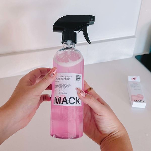 Mack reusable bottle with spray lid and pink liquid inside with a hand attaching label