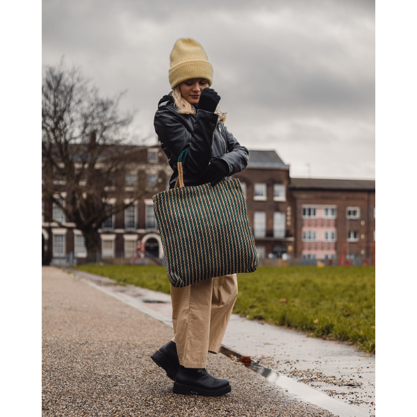 Handwoven jute tote bag in teal and chocolate stripes, being held by a person outside in winter clothing